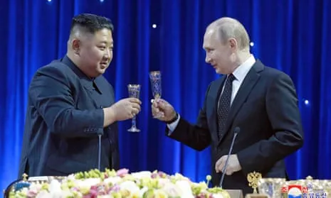 Putin and Jong-Un raise a toast together set in front of a blue curtain